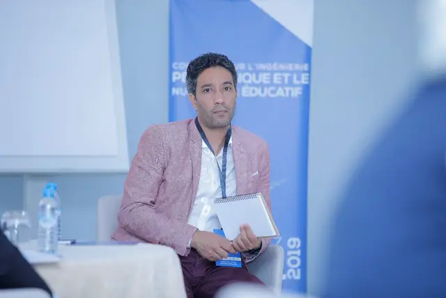 Aziz Mimoudi seated on stage with a tablet at a 2019 conference on instructional design and digital education
