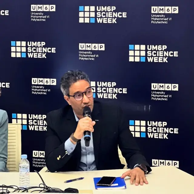Aziz Mimoudi speaking into a microphone in front of a UM6P Science Week backdrop